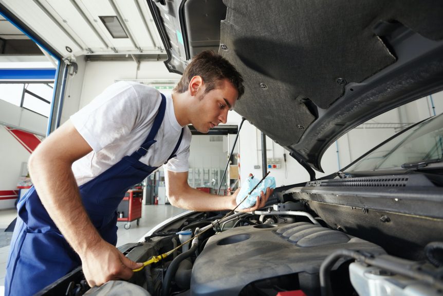 Man Working In Car Repair Shop As Mechanic Reviewing Engine Oil